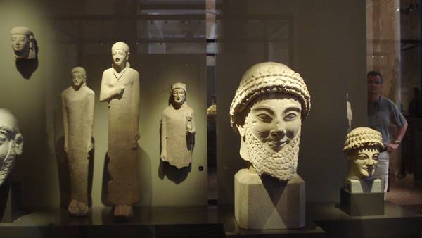 Marble votive statues and bearded head behind glass, Acropolis Museum