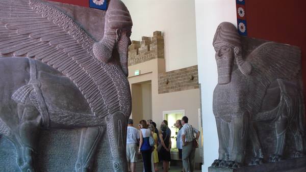 Assyrian winged lamassu stone statues in museum, visitors admire sculptures