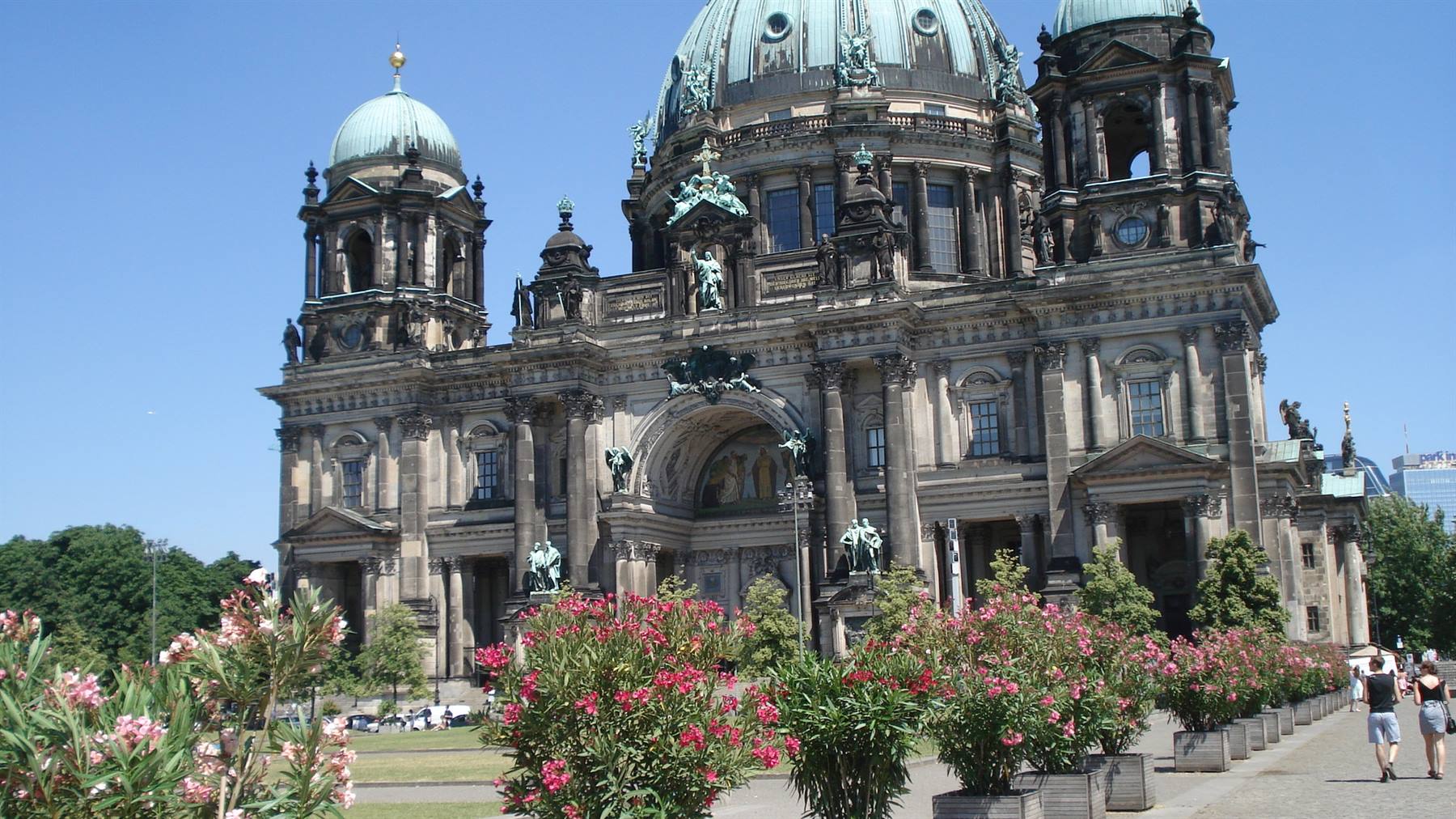 Berlin Cathedral in light stone, green domes, tourists strolling among pink flowers