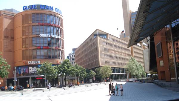 Curved brick building with Saturn and Blue Man Group signs, pedestrians crossing the plaza