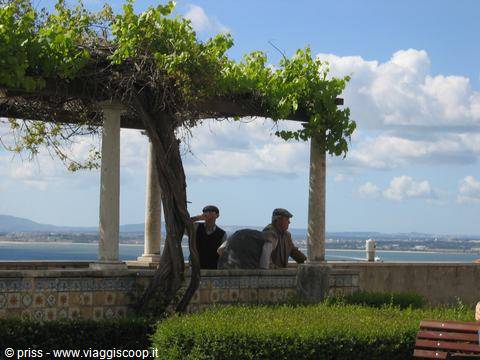 Two men sitting under a stone-and-wood pergola overlooking the river