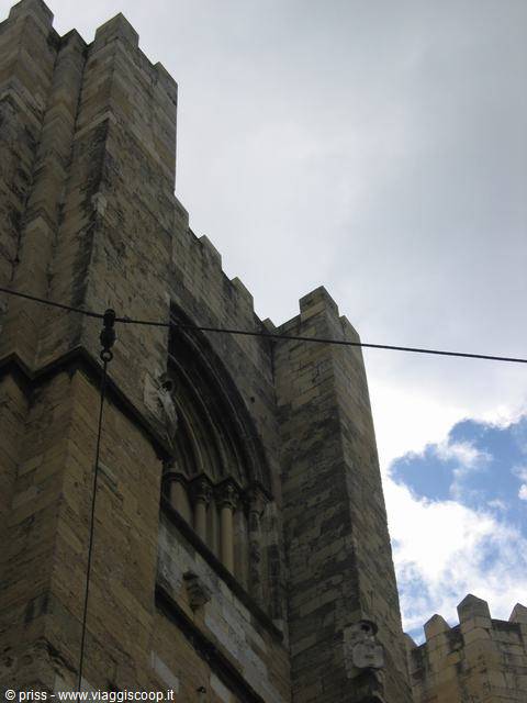 Stone facade with battlements and Gothic window under a cloudy sky