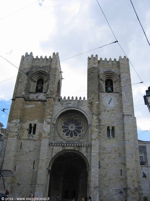 Romanesque facade with twin crenellated towers and stone rose window, tram wires over Lisbon