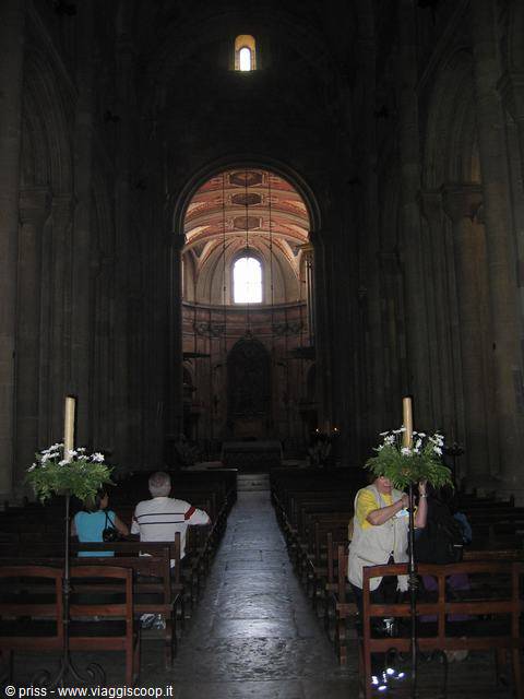 Dim Romanesque cathedral interior, wooden pews and visitors near altar