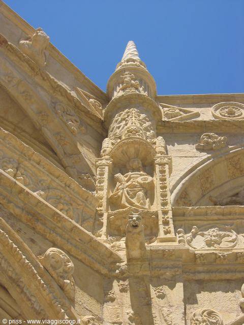 Carved stone saint statue on the Jerónimos Monastery in Lisbon, against blue sky