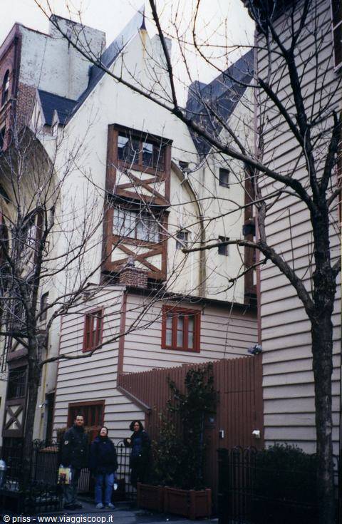 Timber-framed wooden house among New York buildings, bare branches, three passersby