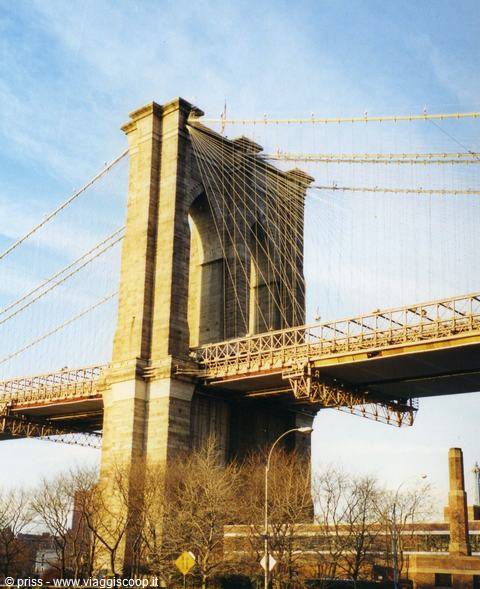 Stone tower of Brooklyn Bridge with steel cables against blue sky