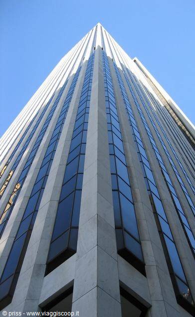 Light stone skyscraper with blue glass windows shot upward against blue sky