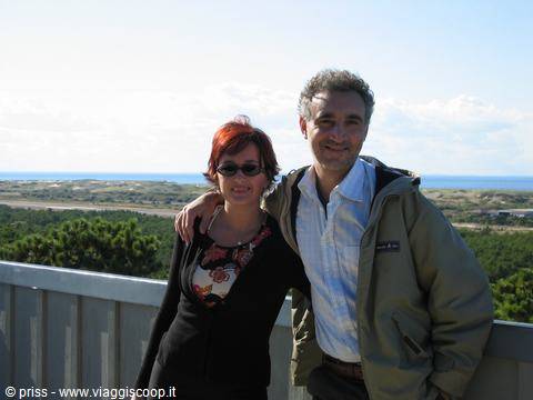 Smiling couple on wooden terrace, dunes and sea in the background