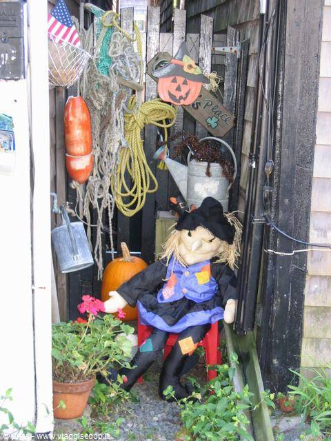Halloween witch doll sitting among pumpkins, fishing ropes and watering cans
