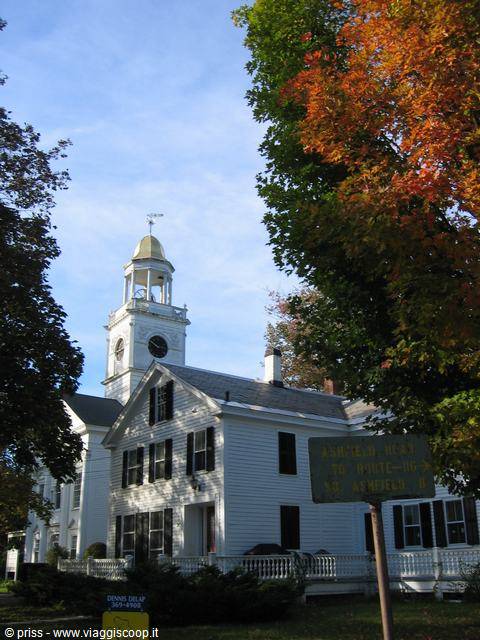 White church with clock tower and golden dome among autumn trees