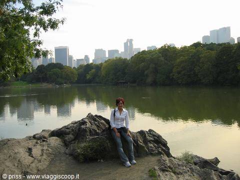 Woman sitting on a rock by Central Park Lake, skyscrapers behind the trees