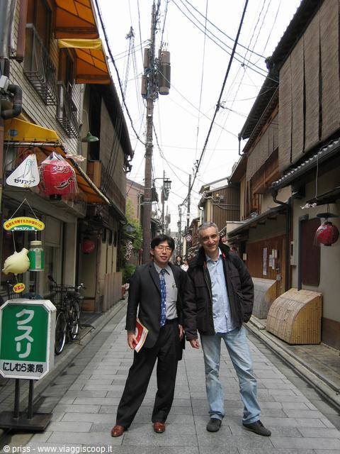 Due amici posano in un vicolo tradizionale di Kyoto tra case in legno e lampioni