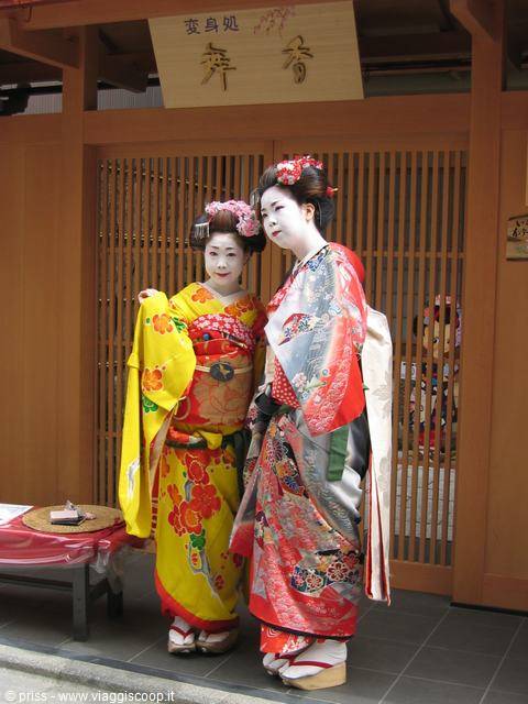 Due maiko in kimono sorridenti davanti a una casa in legno a Kyoto