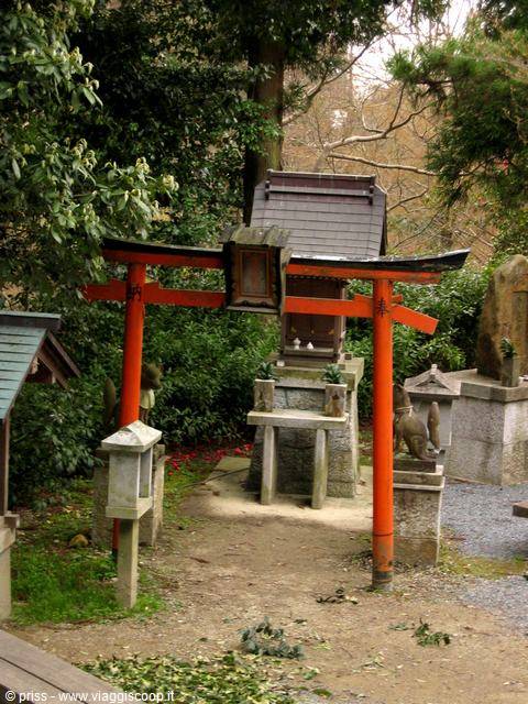 Red torii gates and small stone shrine surrounded by green trees