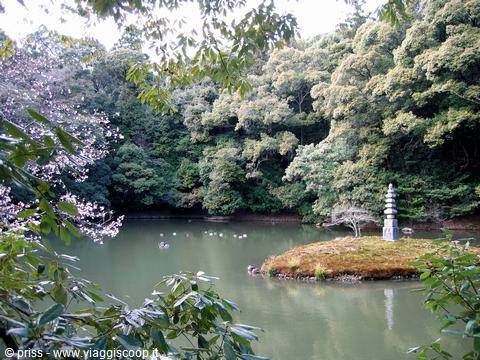 Pagoda in pietra su isolotto nel laghetto del giardino, tra alberi e fiori