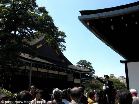 Imperial guard in front of the wooden palace roof, tourists listening under blue sky