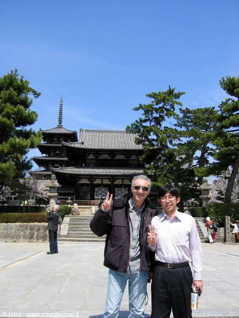 Two men making peace signs before wooden temple hall and pagoda under blue sky
