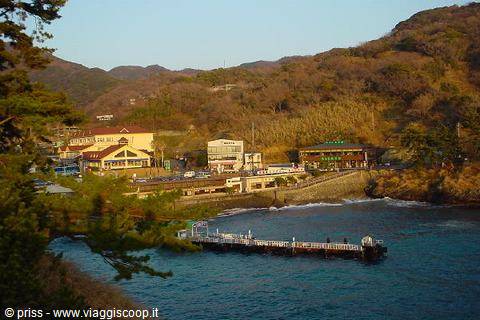 Pier with tourists on turquoise bay, villages and green hills in sunlight