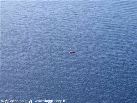 Small red boat alone on vast blue water, daylight