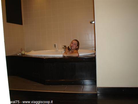 Woman relaxing in a white tiled jacuzzi tub, warm light, hotel bathroom