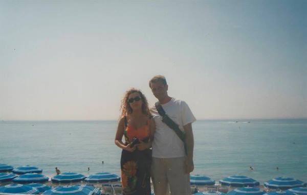 Couple on beach with blue umbrellas, calm sea, bright light