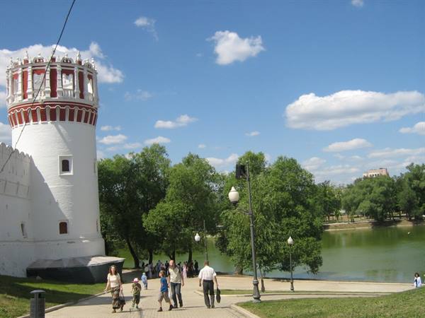 Families stroll past the white and red Novodevichy Convent tower beneath a partly cloudy sky
