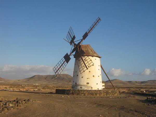 Traditional whitewashed stone windmill with wooden lattice blades among Fuerteventura's arid hills