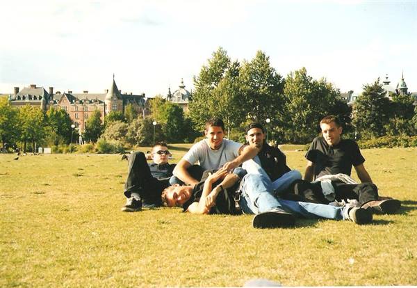 Five friends sitting on park grass with historic buildings and trees behind