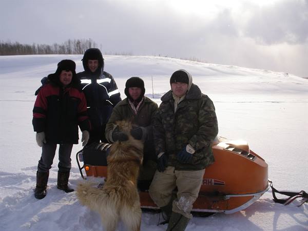 Four men and a dog beside an orange snowmobile on the snow