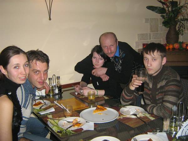 Five friends at a restaurant table with pizza plates and drinks