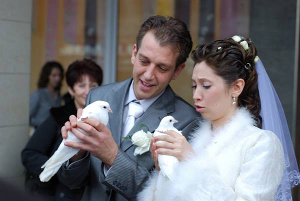Bride and groom in gray and white holding two white doves outdoors