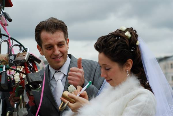 Newlyweds attach a golden padlock to the stand under a grey sky
