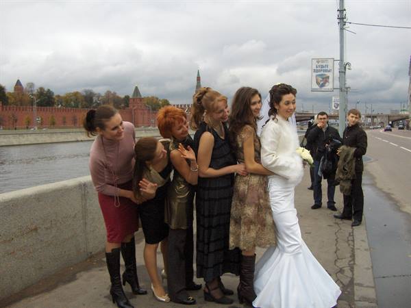 Bride in white gown with friends by the river, Kremlin towers behind