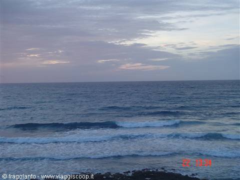 Ocean waves under cloudy sky, dark shore rocks in foreground