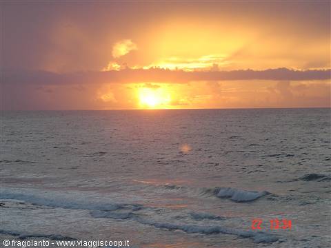 Low orange sun over the ocean, waves on the beach under dark clouds