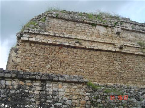 Mayan dry-stone pyramid under a cloudy sky, grass between the blocks