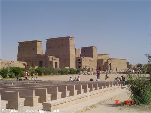 Tourists resting in front of Philae temple, sandstone walls in bright sun