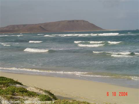 White waves on sandy beach, brown mountain across the sea