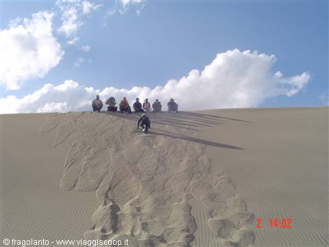 Group of tourists sitting on a sand dune, long shadows, cloudy sky