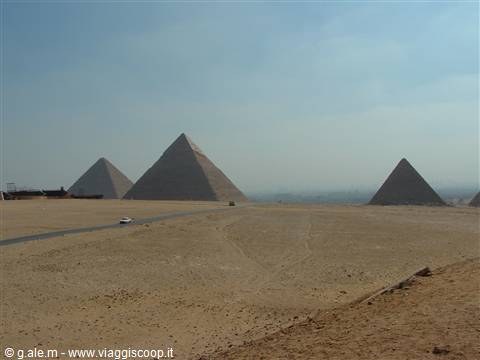 The pyramids of Giza rise from the sand under a hazy sky