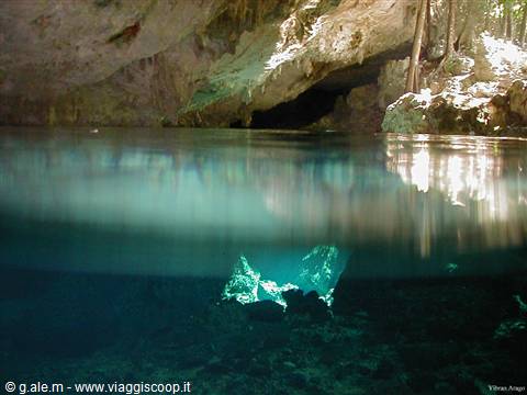 Turquoise water in a cenote, limestone cave with sunlight filtering through rocks