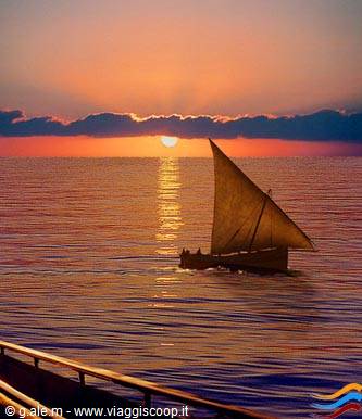 Sailboat with crew glides across calm sea under the low glowing sun