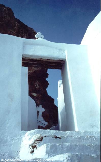 Whitewashed doorway frames dark rock cliff against blue sky