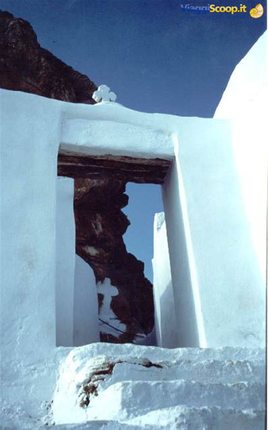 Whitewashed doorway frames dark rock cliff against blue sky