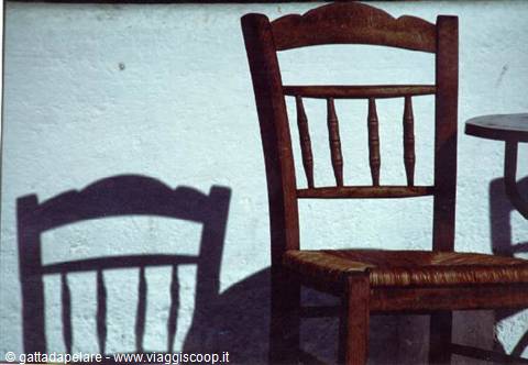 Wooden chair with rush seat against white wall, sharp shadow in sunlight