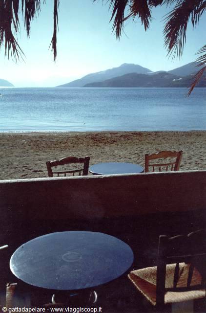 Empty wooden tables by the beach, blue sea and mountains across the bay