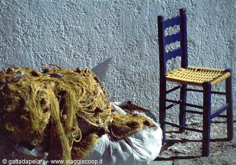 Blue wooden chair with straw seat beside fishing nets against a whitewashed wall