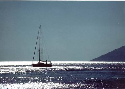 Sailboat silhouetted on sparkling sea, dark mountain on the horizon