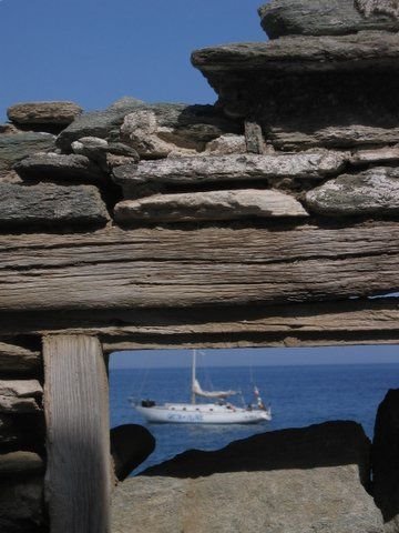 Sailboat framed by weathered stone wall, blue sea in the background
